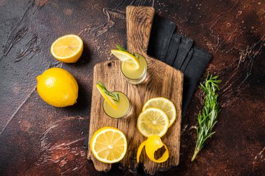 Italian limoncello liqueur and fresh lemons on a rustic wooden board. Dark background. Top view.
