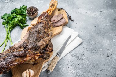 Whole roast mutton lamb leg with spices on a wooden board. Gray background. Top view. Copy space.