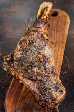 Roast lamb leg meat with herbs and spices on a cutting board. Dark background. Top view.