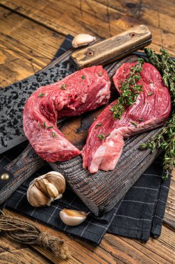 Raw Sirloin flap or Bavette raw beef meat steak on a wooden butcher board with meat cleaver. Wooden background. Top view.