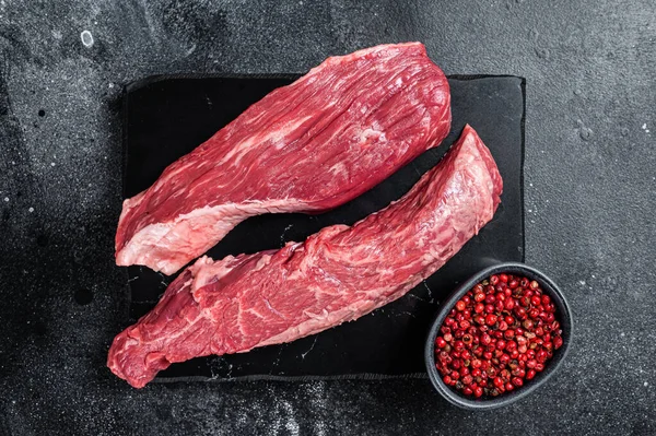 Bavette raw beef meat steak or Sirloin flap on marble board. Black background. Top view.