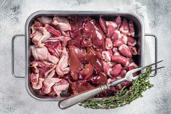 Raw chicken offals meat set, gizzards, stomachs, liver and hearts in a steel tray with herbs. White background. Top view.