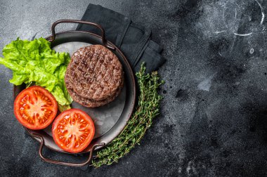 Tasty grilled burger beef patty with tomato, spices and lettuce in kitchen tray. Black background. Top view. Copy space.