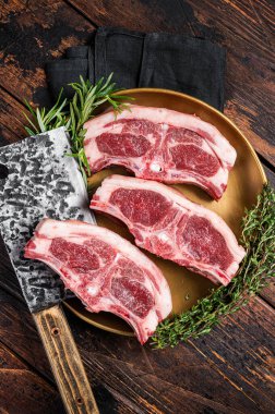 Uncooked Raw lamb loin chops steaks, saddle in plate with rosemary and thyme. Wooden background. Top view.