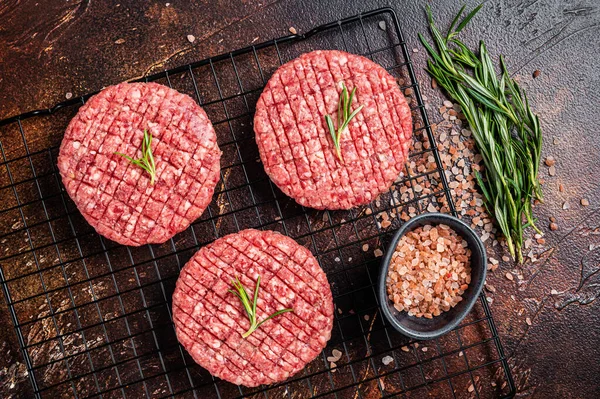 Raw burger cutlet from beef meat with spices and rosemary ready for cooking. Dark background. Top view.