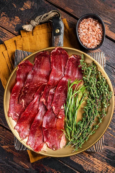 Basturma, sliced dried beef meat, meat Jerky in steel plate with herbs and spices. Wooden background. Top view.