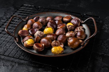 Cracked roast chestnuts served in a tray. Black background. Top view.