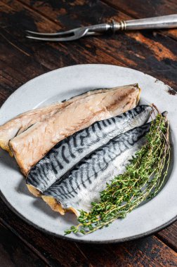 Salty sliced mackerel fillet fish in a plate with herbs. Wooden background. Top view.