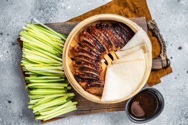 Peking Duck in bamboo steamer served with cucumber, green onion, and wheaten chinese pancakes and sauce Hoysin. Gray background. Top view.