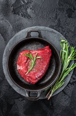 Fresh Raw sirloin rump steak in a skillet with herbs. Black background. Top view.