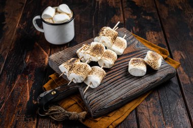 Roasted Marshmallow on the sticks with Cup of coffee on wooden board. Wooden background. Top view.