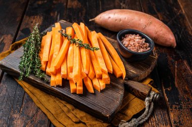 Sweet potatoes on a cutting board, fresh batata french fries ready for cooking. Wooden background. Top view.