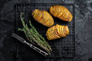 American traditional Homemade Hasselback Potato with Fresh Herbs. Black background. Top view.