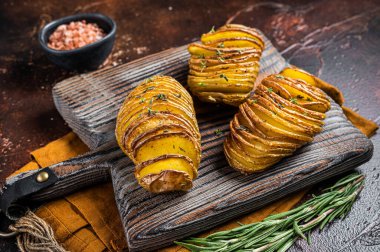 Roasted Hasselback Potato with Fresh thyme and rosemary. Dark background. Top view.