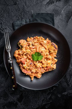 Turkish Menemen, Eggs with tomatoes, green peppers and green onion. Black background. Top view.