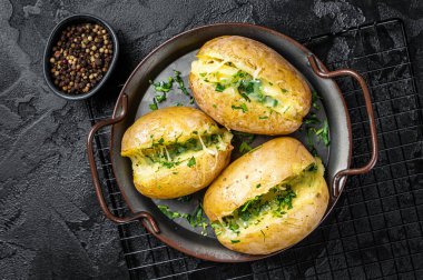 Baked Jacket potatoes with cheese, herbs and butter. Black background. Top view.