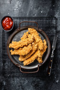 Crispy chicken tenders strips with Ketchup. Black background. Top view.