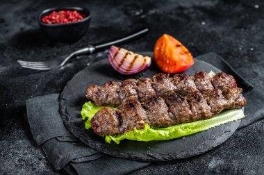 Grilled Urfa kebab with tomato, salad and onion. Black background. Top view.