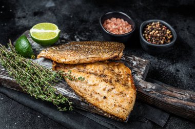 Roast Gilthead Sea Bream fillets with herbs on wooden board. Black background. Top view.