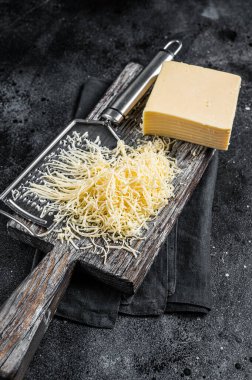 Grated cheese for cooking on a cutting board . Black background. Top view.