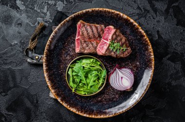 Grilled Oyster Top Blade beef meat steak on a plate with salad. Black background. Top View.