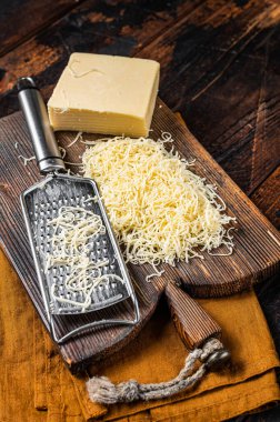 Piece of semi hard cheese and grated cheese with grater. Wooden background. Top view.