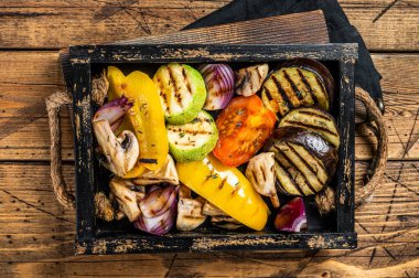Assortment of grilled Vegetables in a wooden box, bell pepper, zucchini, eggplant, onion and tomato. Wooden background. Top view.