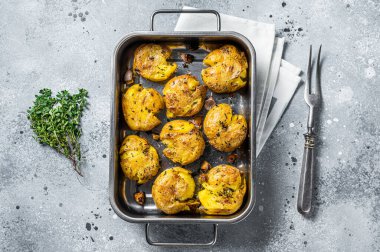 Broken potatoes baked with rosemary and thyme. Gray background. Top view.