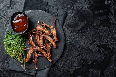 Cooked Spicy fried duck tongue. Black background. Top view. Copy space.