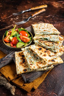 Freshly baked Turkish Gozleme, flatbread with greens and cheese. Dark background. Top view.