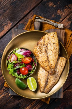 Roasted Gilthead Sea Bream fillets served with fresh vegetable salad. Wooden background. Top view.