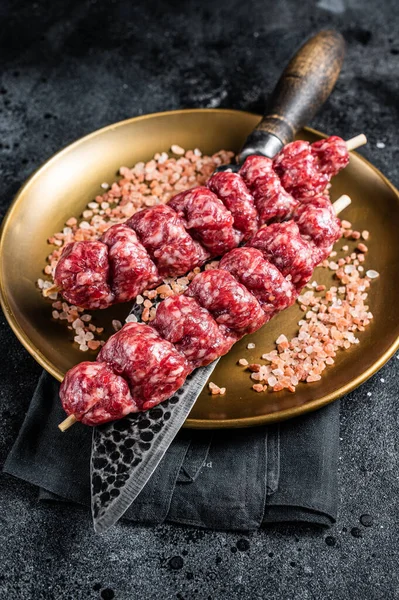 Raw kofta, kofte kebab Skewers with beef and lamb meat and spices. Black background. Top view.