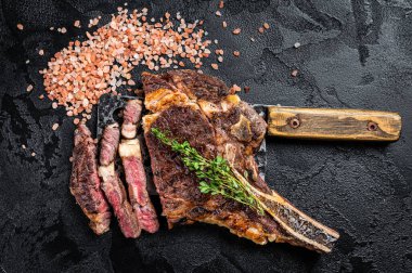 Dry aged grilled Tomahawk or cowboy beef meat steak on a meat cleaver. Black background. Top view.