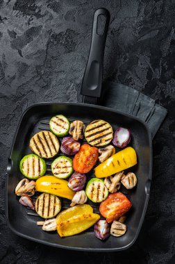 Vegetables grilled in a grill skillet, bell pepper, zucchini, eggplant, onion and tomato. Black background. Top view.