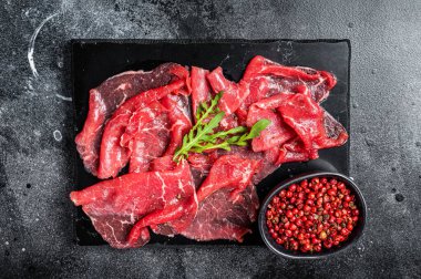 Slices of Beef Capriccio, raw marbled meat. Black background. Top view.