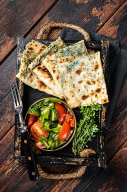 Baked Gozleme flatbread with greens in a box with vegetable salad. Wooden background. Top view.