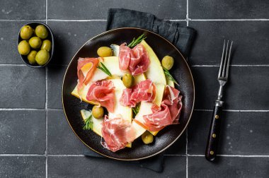 Prosciutto ham and melon salad in a plate. Black background. Top view.