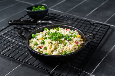 Asian Fried rice with egg and vegetables in a skillet. Black background. Top view.