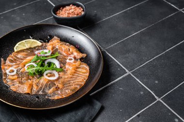 Tabağında soğan ve roka olan taze somon carpaccio. Siyah arka plan. Üst Manzara. Boşluğu kopyala.