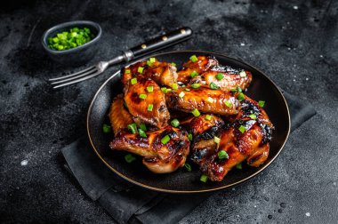 Baked chicken wings with sweet chili sauce in a plate. Black background. Top view.
