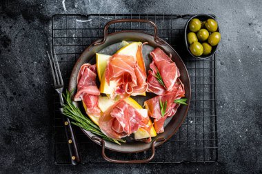 Italian prosciutto parma with melon and fresh rosemary. Black background. Top view.