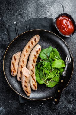 BBQ Grilled pork sausages served with greens. Black background. Top view.