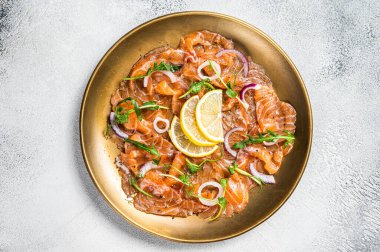 Fresh raw salmon carpaccio slices with onion and arugula served on a plate. White background. Top view.