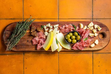 Meat cheese platter antipasti snack with Prosciutto ham, Parmesan, Blue cheese, Melon and Olives on wooden board. Black background. Top view.