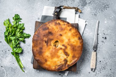 Ossetian pie with beef meat and herbs on wooden board. Gray background. Top view.