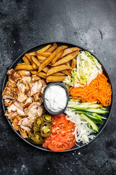 Shawarma Doner kebab on a plate with french fries and salad. Black background. Top view.