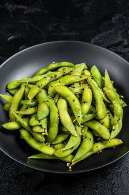 Boiled Edamame Soy Beans with sea salt in a plate. Black background. Top view.