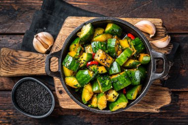 Chinese Smashed Cucumber salad pai huang gua in a skillet. Wooden background. Top view.