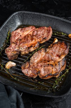 Grilled Pork steaks, neck meat on grill pan. Black background. Top view.