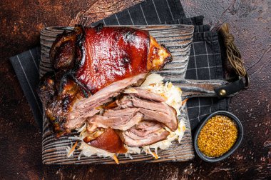 Schweinshaxe Roasted Pork Ham Hock, knuckle with Sauerkraut served on a wooden board. Dark background. Top view.